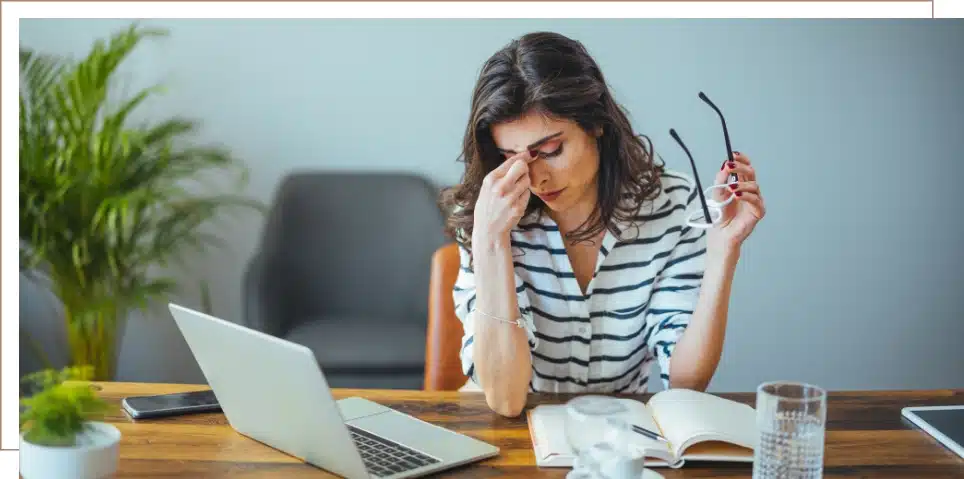 A woman showing she is overtired by holding her head while working at a desk